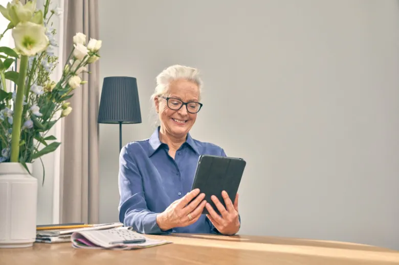 Starší žena s brýlemi používá digitální tablet v interiéru.