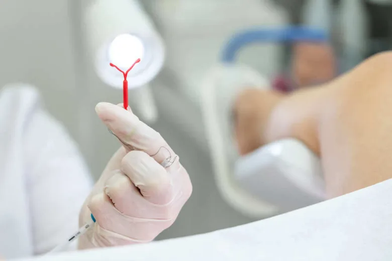 Ruka v rukavici drží nástroj pro zavedení nitroděložního tělíska s kapkou krve.
