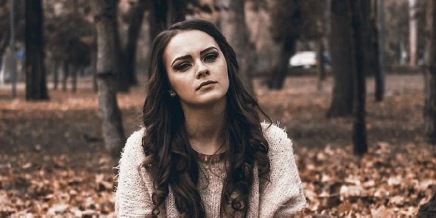Žena stojí v parku s podzimními listy na zemi.