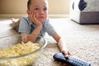 Chlapec leží na koberci s popcornem a dálkovým ovladačem
