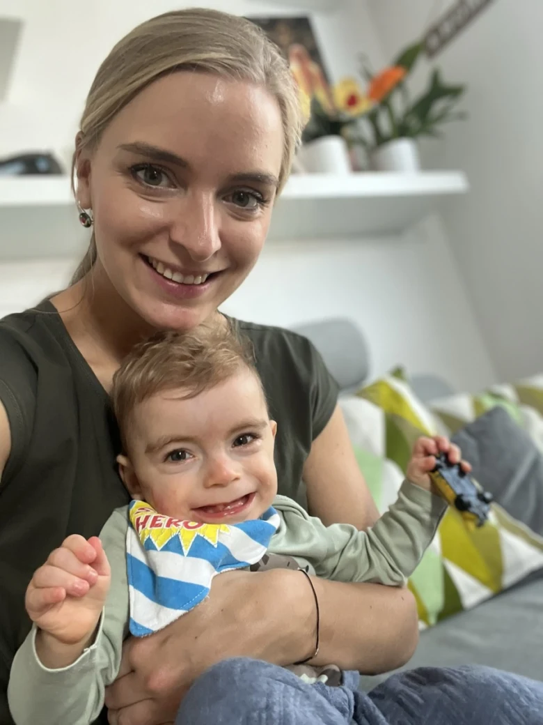 Žena drží v náručí šťastného malého chlapce s bílým šátkem.