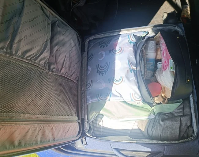 Otevřená taška s oblečením a kosmetikou včetně možných nosních kapek.
