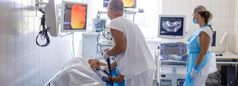 Lékaři vyšetřují pacienta v nemocničním prostředí s monitorovými přístroji.