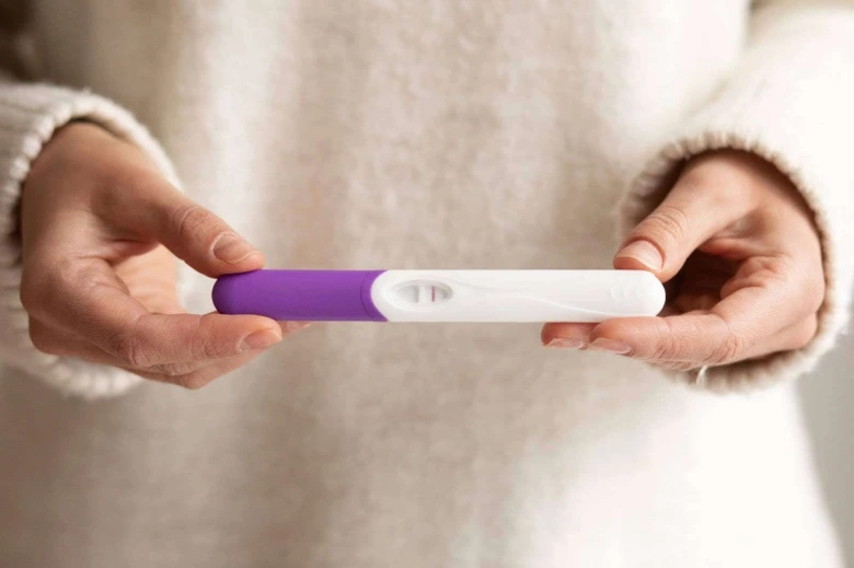 Žena drží pozitivní těhotenský test s dvěma čarami.