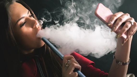 Žena kouří elektronickou cigaretu a fotí se telefonem.
