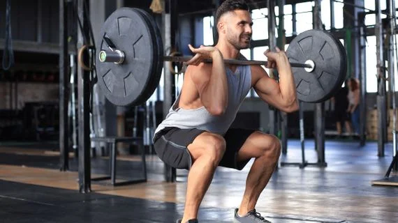Muž dělá cvičení s činkou v posilovně pro zrychlení metabolismu