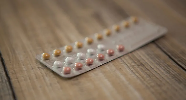 Blister s balíčkem antikoncepčních pilulek různých barev na dřevě.