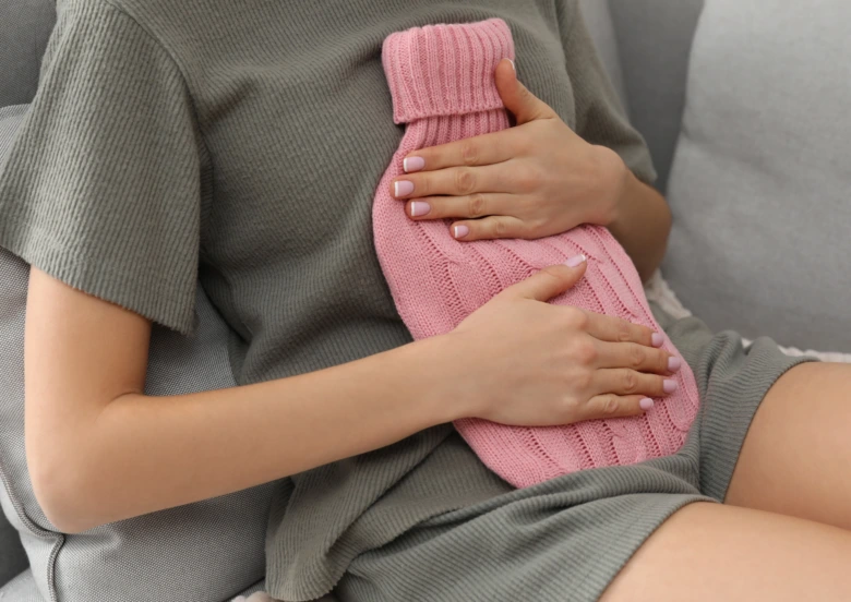 Žena drží horkou vodu na břiše pro úlevu od menstruačních bolestí.