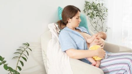 Matka kojí dítě na gauči v klidném domovním prostředí.