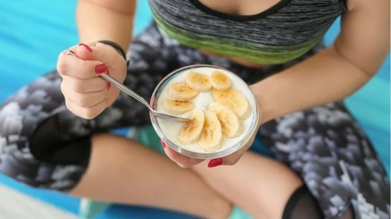Žena v sportovní oblečení jí jogurt s banány.