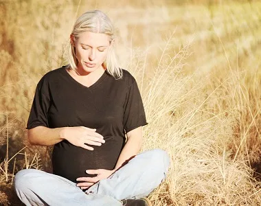 Těhotná žena sedí venku a drží si břicho.